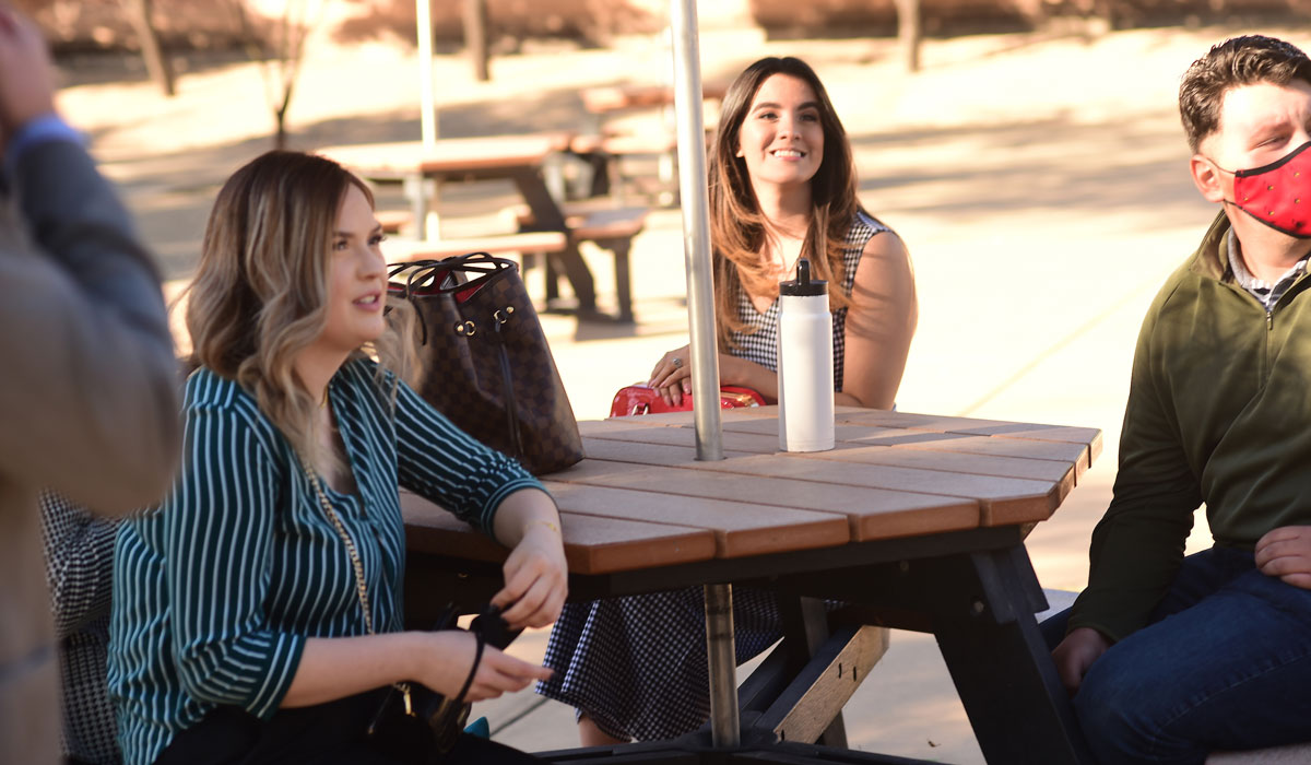 Tres estudiantes sentados en mesa de picnic riendo